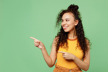 Wall Mural - Young happy woman of African American ethnicity wear yellow tank shirt top point index finger aside on area mock up isolated on plain pastel light green background studio portrait. Lifestyle concept.