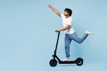 Wall Mural - Full body young happy Indian man he wear white t-shirt casual clothes ride electric scooter do flying super hero gesture isolated on plain pastel light blue cyan background studio. Lifestyle concept.