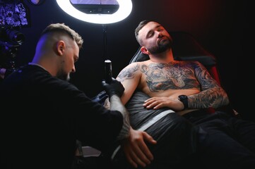 Wall Mural - Portrait of a tattoo master showing a process of creation tattoo on a hand under the lamp light