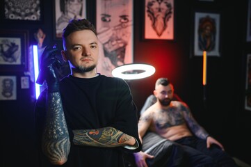 Wall Mural - tattooer in black gloves dreamily looking in camera holding tattoo machine in hand in modern tattoo studio