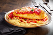 Chicken Parmesan, Italian pasta dish. Breaded chicken breast with cheese and spaghetti with tomato sauce, with parsley, on a wooden table