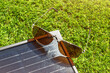 The alternative energy generation with solar panel. The set of solar panel an sunglasses on the green grass background.
