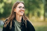 Fototapeta Niebo - Portrait of a smiling young girl with glasses in the park. High-quality photo
