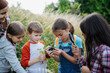 © Halfpoint - Young students learning about nature during biology field teaching class, observing wild plants with magnifying glass and pocket microscope. Dedicated teachers during outdoor active education.