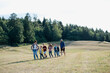 © Halfpoint - Young students walking across meadow during biology field teaching class, holding hands. Dedicated teachers during outdoor active education teaching about ecosystem, ecology.