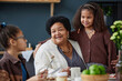 Portrait of happy African American grandmother with two girls enjoying time together in kitchen