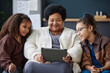 Front view portrait of smiling senior Black woman using digital tablet at home with two young girls helping