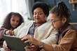 Side view portrait of teenage Black girl teaching grandmother using digital tablet at home