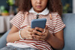 Close up of young Black girl holding smartphone in hands and browsing internet or playing mobile game copy space