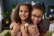 Portrait of two African American girls as sisters embracing and looking at camera at home