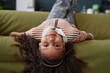 Portrait of young Black girl lying upside down on sofa at home and looking at camera copy space