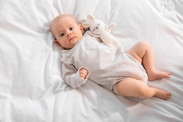 Canvas Print - Cute little baby with toy lying on white sheets, top view