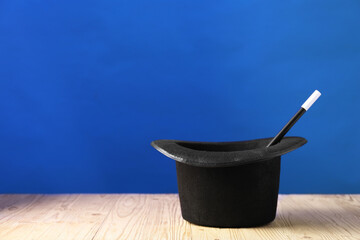 Wall Mural - Magician's hat and wand on wooden table against blue background, space for text