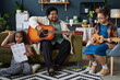 Full length portrait of Black senior woman with two young girls playing musical instruments together indoors
