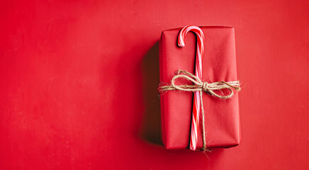 Wall Mural - Christmas gift box wrapped in red paper tied with twine with candy cane on re background. Holiday presents shopping celebration concept