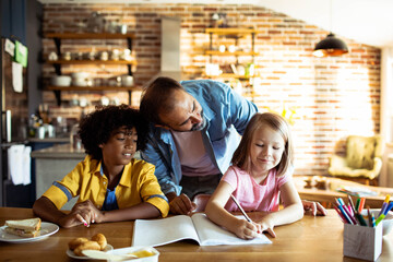 father helping children with homework at kitchen table