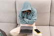 © Vitaliy - Young woman in hoodie sits on the couch and works at laptop