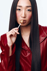 Wall Mural - Attractive woman enjoying a lollipop in front of a white background with long black hair and red jacket