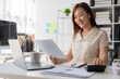 © MrAshi - Beautiful Asian female accountant smiling while working with laptop and documents about finance, mathematics, accounting reports, statistics. and research ideas
