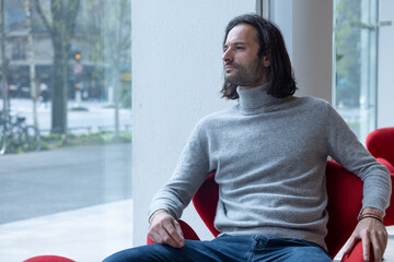 Poster - portrait d'un bel homme brun aux cheveux longs qui est assis dans le bureau de son entreprise. Il est sympathique et souriant