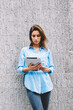 © BullRun - Pensive hipster girl reading e-book standing outdoors near promotional background with copy space area for your text message.Young woman watching tutorial on website on modern touch pad device