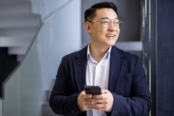 a professional asian businessman smiling joyfully while using his mobile phone in the contemporary s