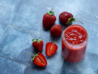 Wall Mural - a glass of strawberry smoothie and ripe strawberries on a blue table