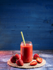 Wall Mural - a glass of homemade strawberry smoothie with a straw on a blue table, copy space