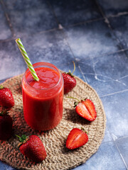 Wall Mural - a glass of homemade strawberry smoothie with a straw on a blue table, copy space