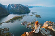 Woman tourist traveling in Norway active summer vacations adventure lifestyle outdoor in Lofoten islands, girl on cliff edge enjoying sea aerial view from Reinebringen mountain top