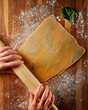 Hands roll out homemade egg pasta with rolling pin