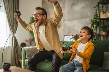 Father and son play video games with joystick and have fun at home