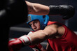 Young boxer with protective helmet or shield on head looking at his rival during kick while both fighting on ring at sparring round