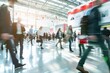 © Ilia Nesolenyi - Individuals walking briskly through a spacious trade fair hall, captured in motion blur