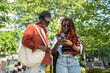 Concerned African American woman focused on smartphone with man stopped on sidewalk to look at map app while walking together. Confused couple looking for information on cell phone standing in city.