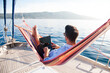 Working in sea traveling. Man with laptop in beach hammock. Summer vacation, living on yacht. Successful freelancer using computer. Workplace on nature outdoors, home office. Business lifestyle