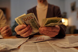 Fototapeta  - Hands of unrecognizable elderly woman sitting by table with paid and unpaid financial bills and counting dollar banknotes