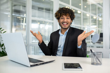 Wall Mural - Cheerful young businessman with curly hair shrugs humorously during a presentation in a bright, modern office setting. Emphasizing a light-hearted approach to business communications.