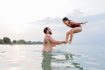 Wall Mural - side view at happy girl jumping in the water from the father arms