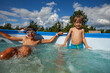 Cheerful youngsters having fun in water pool during sunny day