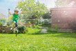 A cheerful boy skips over the spray from sunny lawn sprinkler