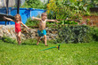 Two joyful kids running through sprinkler on sunny day in garden