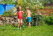 Two joyful kids wear swimsuits play in a sunny backyard garden