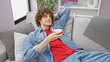 A relaxed young man with curly hair enjoying coffee in a modern living room, exuding casual comfort and style.