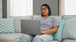 © Krakenimages.com - A middle-aged hispanic woman working on a laptop in a modern living room setup, focused and comfortable.