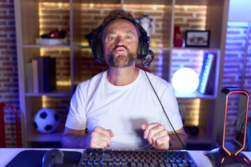 Poster - Middle age man with beard playing video games wearing headphones looking at the camera blowing a kiss on air being lovely and sexy. love expression.