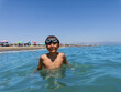 A smiling young swimmer with goggles take pleasure in clear sea