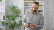 © Krakenimages.com - Smiling senior hispanic man with grey beard using smartphone in modern office.