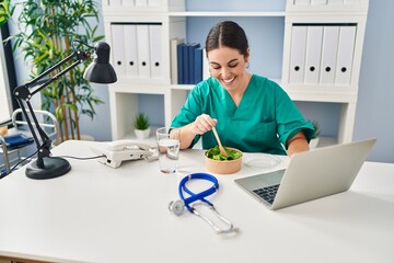 Wall Mural - Young beautiful hispanic woman doctor eating salad working at clinic