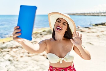 Wall Mural - Young beautiful hispanic woman tourist smiling confident having video call at seaside